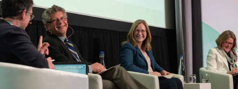 Panel discussion with speakers seated on stage in armchairs during a conference event.