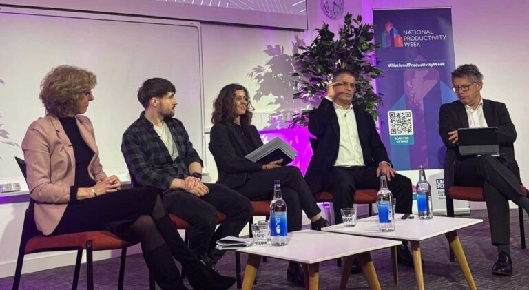 Panel discussion at a National Productivity Week event, with speakers seated on stage in front of presentation screens.